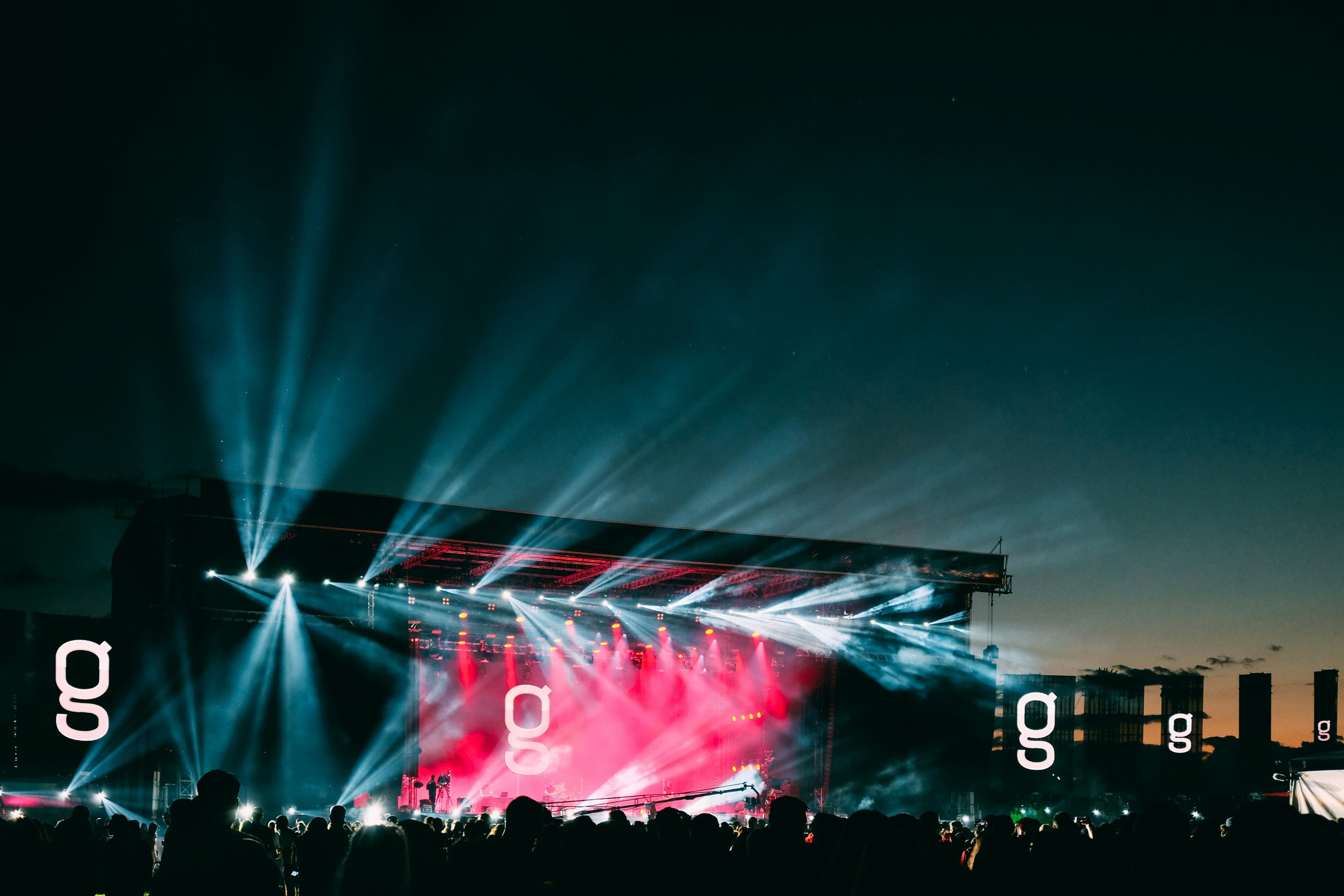 Silhouettes of a crowd at an outdoor music festival stage lit up with colorful lights at night