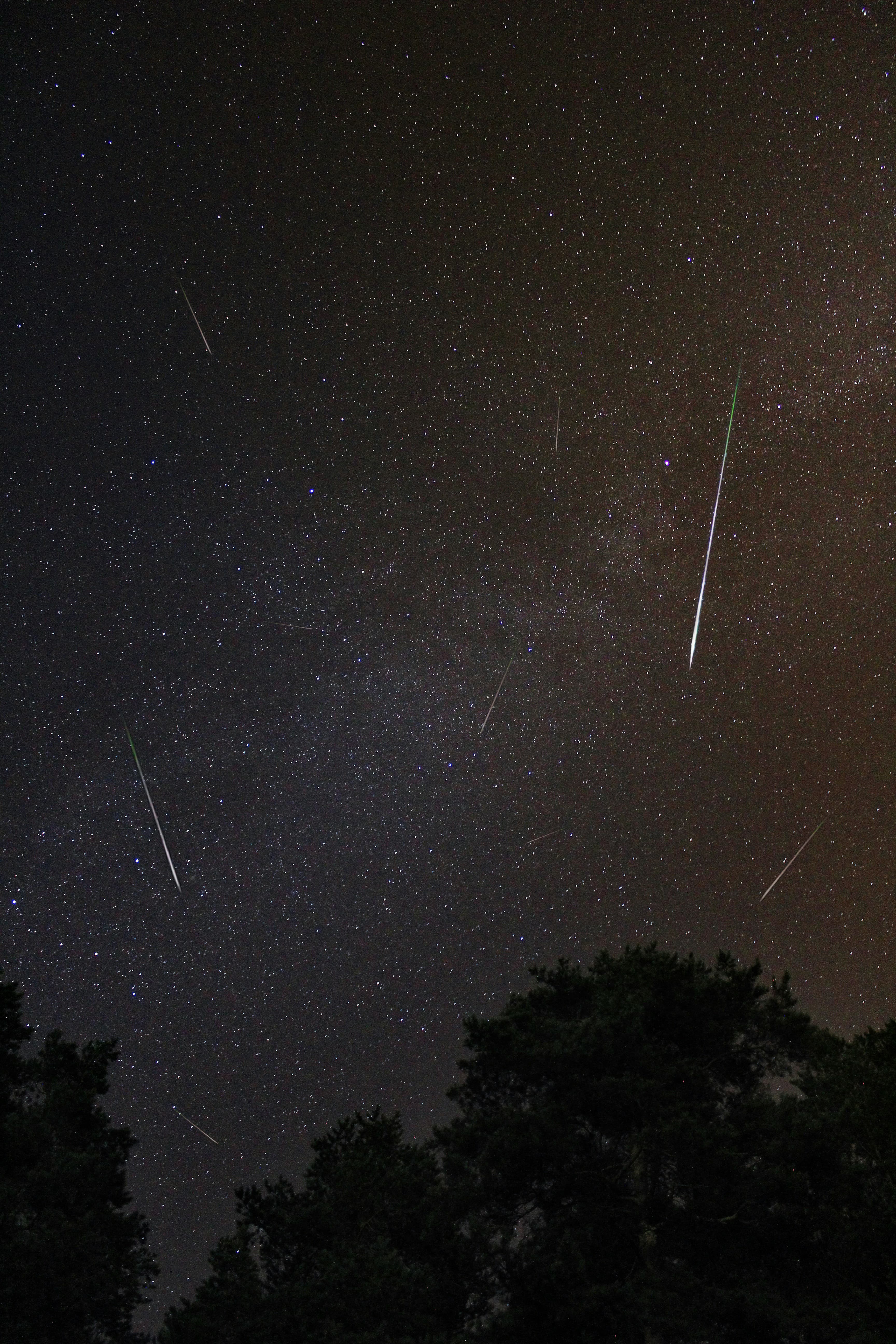 Bright meteor streaking across a star-filled night sky above a dark, open landscape
