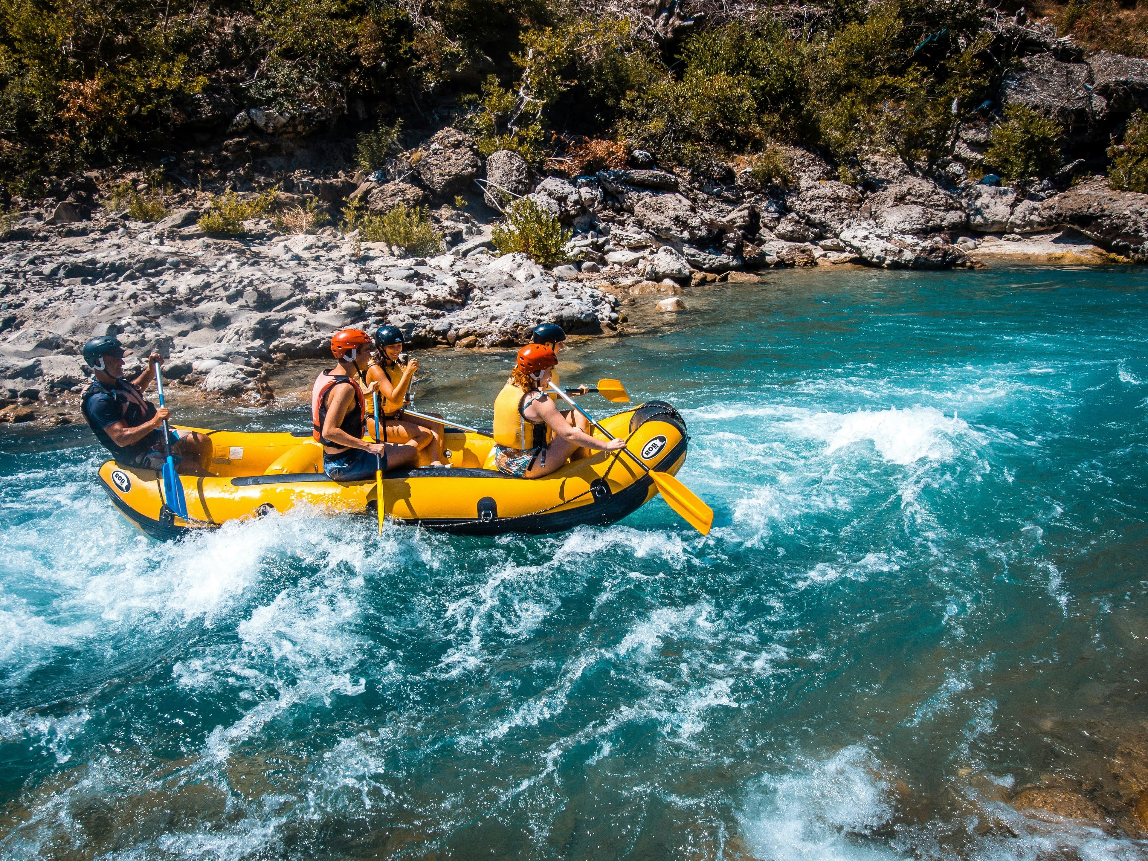 A group rafting down a river on an inflatable raft, surrounded by mountainous, forested terrain