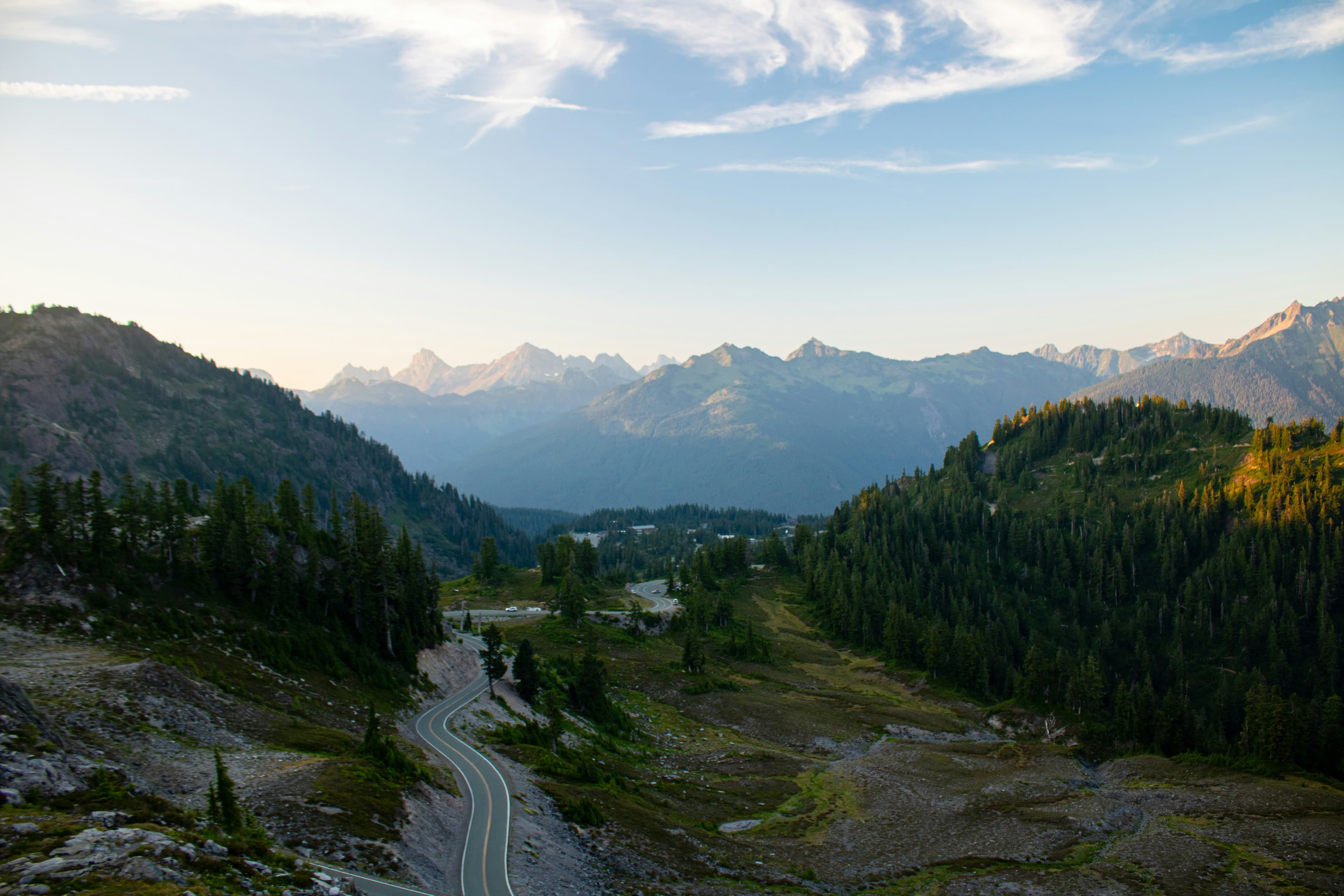 A winding two-lane mountain highway cuts through dense evergreen forest with forested slopes on both sides